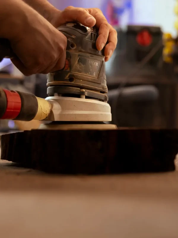 Carpenter using orbital sander with fine sandpaper on lumber piece to achieve refined finish. Manufacturer using angle grinder on wood block for professional results, close up shot